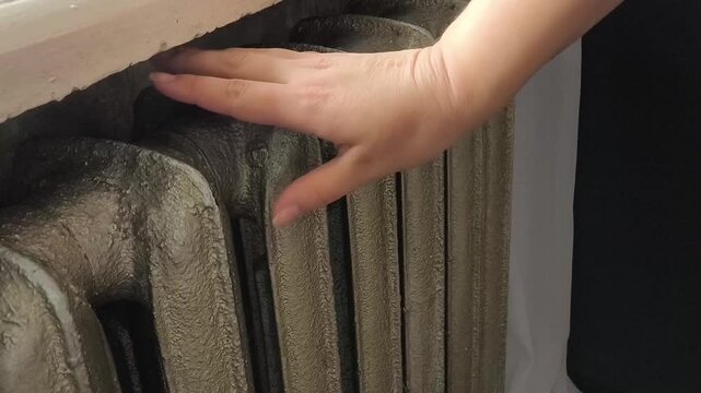 A woman warms her hands near an old heating radiator in the house. Old cast iron radiators in the house