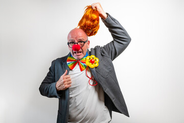 Man removing orange wig revealing bald head with clown nose