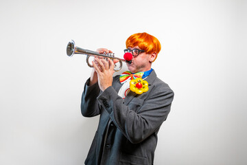 Clown playing trumpet with bright orange wig and red nose