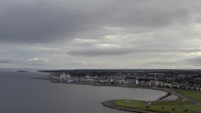 Aerial orbit establishing Salthill coastline at evening, with dramatic skies over Galway Bay, Ireland.