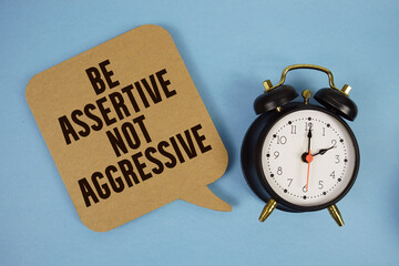 Be Assertive Not Aggressive text with alarm clock on blue background