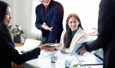 Diverse team of young professionals collaborating in a bright modern office, discussing business data on tablets and laptops.