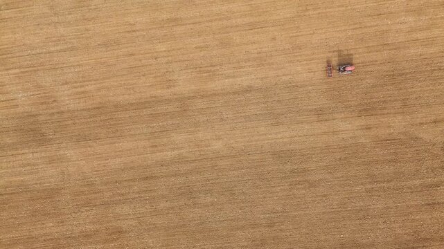 Vintage crawled tractor is leveling plowed soil in a vast, brown field