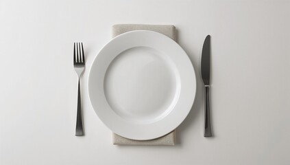 Empty white dinner plate set for a formal meal with a stainless steel fork and knife resting on a simple beige linen napkin above a clean bright surface