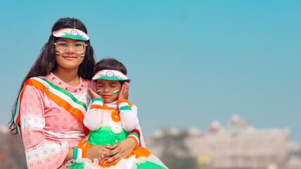 Portrait of two happy Indian sisters (teenager and toddler) dressed in tricolor clothes sitting...