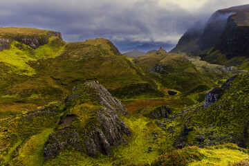 Dramatic green hills of the Quiraing on Isle of Skye under moody cloudy sky, rugged Scottish highlands landscape with deep valleys and rocky formations, wild nature travel concept.