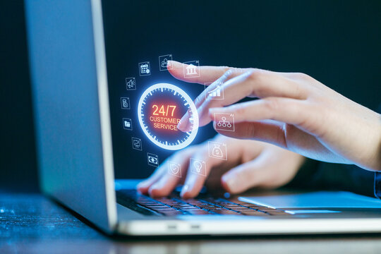Hands typing on a laptop displaying digital icons representing 24 7 customer service at a workspace - Powered by Adobe