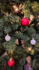 Close-up of a Christmas tree decorated with red and white balls and glowing warm fairy lights.