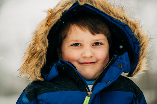 Young boy smiling wearing blue winter parka with fur hood