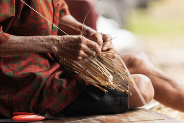 Skillful senior artisan weaving traditional bamboo basket in Thailand