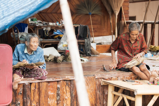 Two elderly artisans weaving on wooden porch