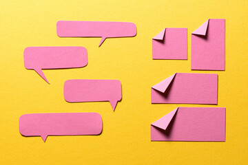 Pink speech bubbles and paper memo notes with folded dog-ear earmark and copy space for text on yellow background, communication dialog concept top view flat lay
