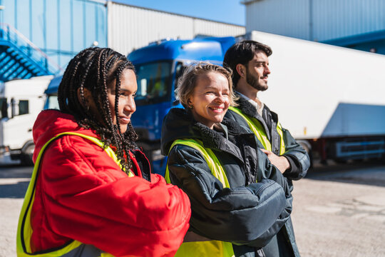 Diverse team of smiling truck drivers standing with arms crossed at a loading dock, ready for work in a cold storage facility