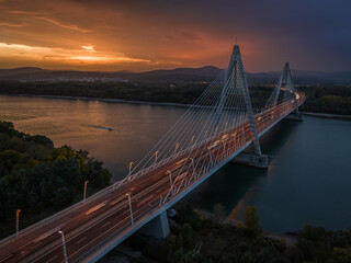Fototapeta premium Budapest, Hungary - Aerial view of the cable-stayed Megyeri Bridge over River Danube at dusk with beautiful dramatic golden sunset sky and Buda Hills at background