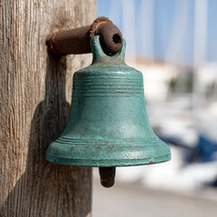 Obraz premium An antique bell mounted on a wooden post near a blurred marina.