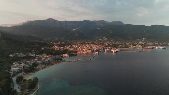 Wide aerial circle pan around Limenas town and port on Thasos Island, Greece, capturing the stunning Aegean Sea coastline during a golden summer sunrise.