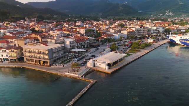 Aerial drone circle shot of the picturesque Limenas waterfront, harbor, and town on Thasos Island, Greece, illuminated by the summer sunrise.
