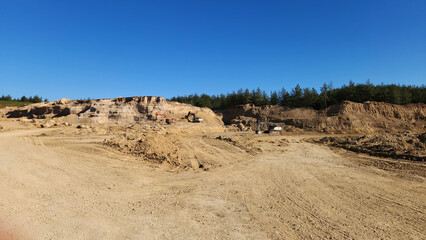 Heavy machineries excavating fill soil at a construction site under a clear blue sky