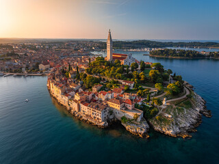 Rovinj, Croatia - Aerial view of the old town of Rovinj with Church of St. Euphemia and rising sun on a summer morning in Istria, Croatia. Golden sky and red rooftops by the Adriatic sea
