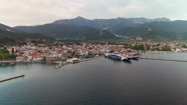 Aerial drone descent towards Limenas port and coastal town, Thasos Island, Greece, illuminated by the warm light of a tranquil summer morning.