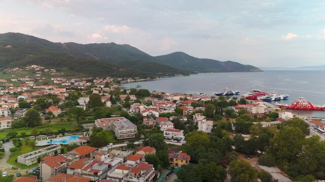 Scenic aerial pan across Limenas port, Thasos Island, Greece, showcasing the coastal town and Aegean Sea at golden summer dawn.