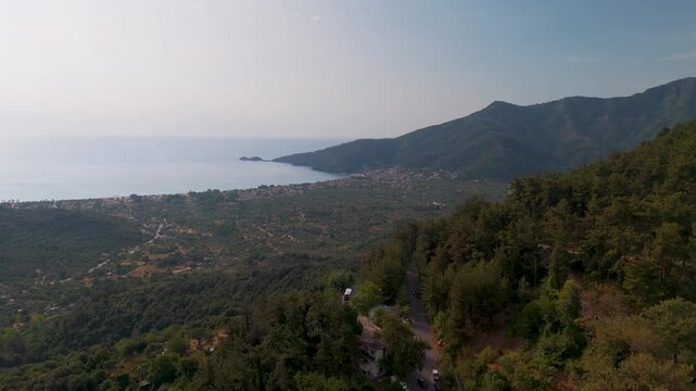 Winding mountain road ascending the dense forest slopes of Mount Ipsarion near Panagia village on Thasos Island, Greece - Aerial view.