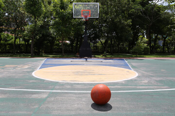 Basketball on outdoor court with hoop and green trees background under bright sunlight