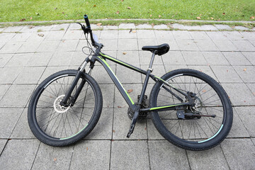 Black and green mountain bike on concrete pavement tiles in city park with green grass background
