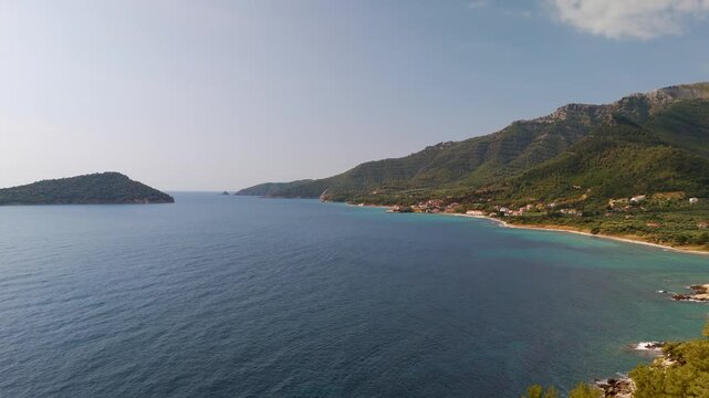 Wide aerial drone shot over the Aegean Sea showing the lush forested coast of Thasos Island near Kinira village and the beautiful Nisida Kinira islet in Greece.