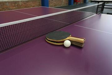 Two table tennis rackets and a white ball on a purple ping pong table background