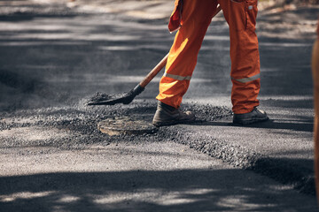 Construction worker working on a new asphalt layer on a public street.