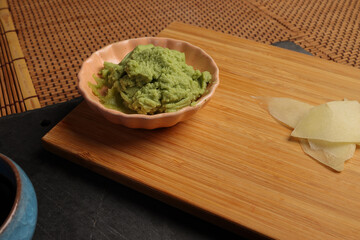 Traditional wasabi sushi sauce in a small dish, featuring a vibrant green color and smooth texture on wooden bad bamboo mat