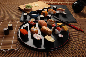 High-quality close-up of fresh assortment sushi rolls served on a dark plate, featuring vibrant colors, fresh fish, laid on slate board bamboo mat chopsticks