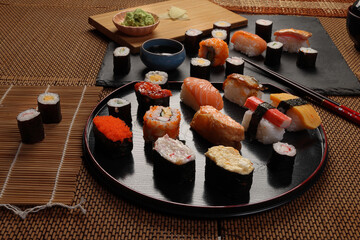 High-quality close-up of fresh assortment sushi rolls served on a dark plate, featuring vibrant colors, fresh fish, laid on slate board bamboo mat chopsticks