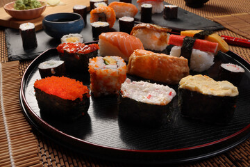 High-quality close-up of fresh assortment sushi rolls served on a dark plate, featuring vibrant colors, fresh fish, laid on slate board bamboo mat chopsticks