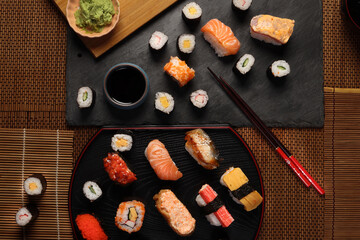 High-quality close-up of fresh assortment sushi rolls served on a dark plate, featuring vibrant colors, fresh fish, laid on slate board bamboo mat chopsticks