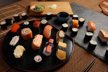 High-quality close-up of fresh assortment sushi rolls served on a dark plate, featuring vibrant colors, fresh fish, laid on slate board bamboo mat chopsticks