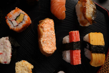 High-quality close-up of fresh assortment sushi rolls served on a dark plate, featuring vibrant colors, fresh fish, laid on slate board bamboo mat chopsticks