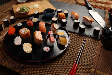 High-quality close-up of fresh assortment sushi rolls served on a dark plate, featuring vibrant colors, fresh fish, laid on slate board bamboo mat chopsticks