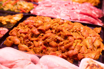 Marinated chicken pieces in curry are displayed in display case. Butcher shop sells fresh meat products, semi-finished products
