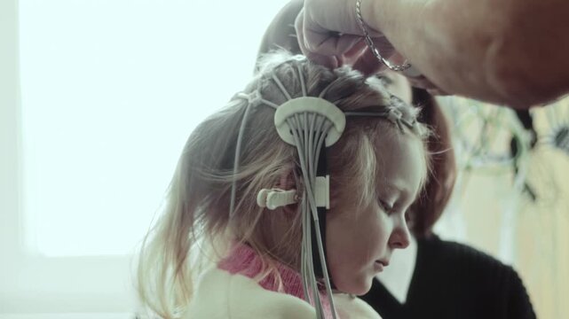 Close-up of nurse attaching contact pads to Electroencephalography electrode cap on head of 4 years old Caucasian child during brain activity diagnostic test in medical clinic. Mother parent