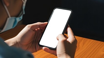 Person in face mask holding smartphone with blank white screen.