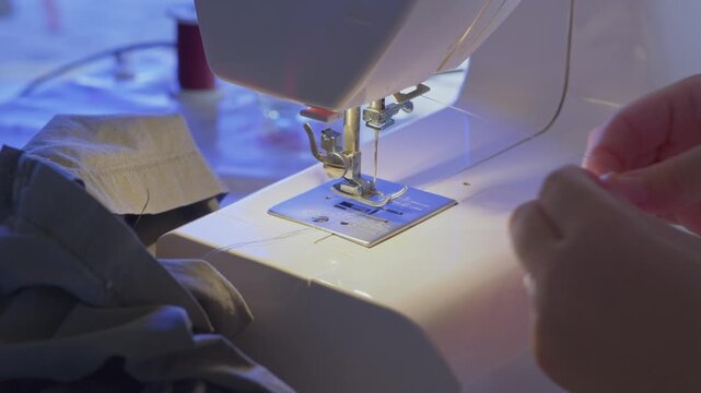 Skilled tailor threading a sewing machine needle in a cozy workshop, closeup of hands preparing thread for precise garment sewing, tailoring and dressmaking craft