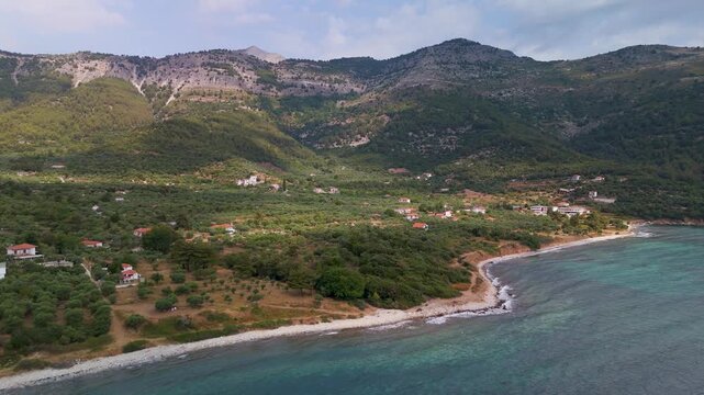 Establishing aerial drone view of the picturesque Kinira coastline, Thasos, Greece, highlighting the dense forest slopes meeting the bright Aegean Sea beaches on a summer morning.