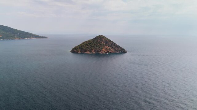 Scenic aerial drone approach toward Nisida Kinira Islet off the lush coast of Thasos, Greece, overlooking the turquoise Aegean Sea.