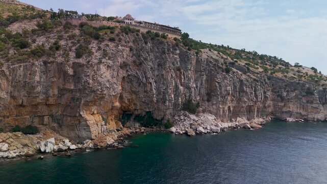 Drone shot flying up a sheer cliff face toward the Holy Monastery of the Archangel Michael landmark on Thasos Island, Greece.
