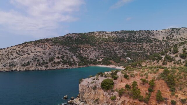 Aerial drone approach to the secluded Arsanas Beach on the rocky coast of Thasos Island, Greece, highlighting the turquoise Aegean Sea.