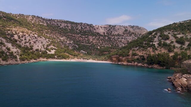 Aerial drone approach to the secluded Arsanas Beach on the rocky coastline of Thasos Island, Greece, highlighting the turquoise Aegean Sea and rugged cliffs.