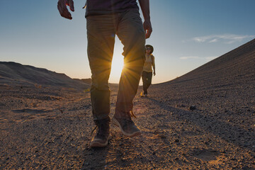 A couple walks a dirt road in the Mongolian desert as the sun sets during golden hour. They approach the camera, their long shadows stretching across the ground behind them.