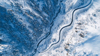 Snow-covered mountains frame a winding road alongside a river during winter season at a high altitude location